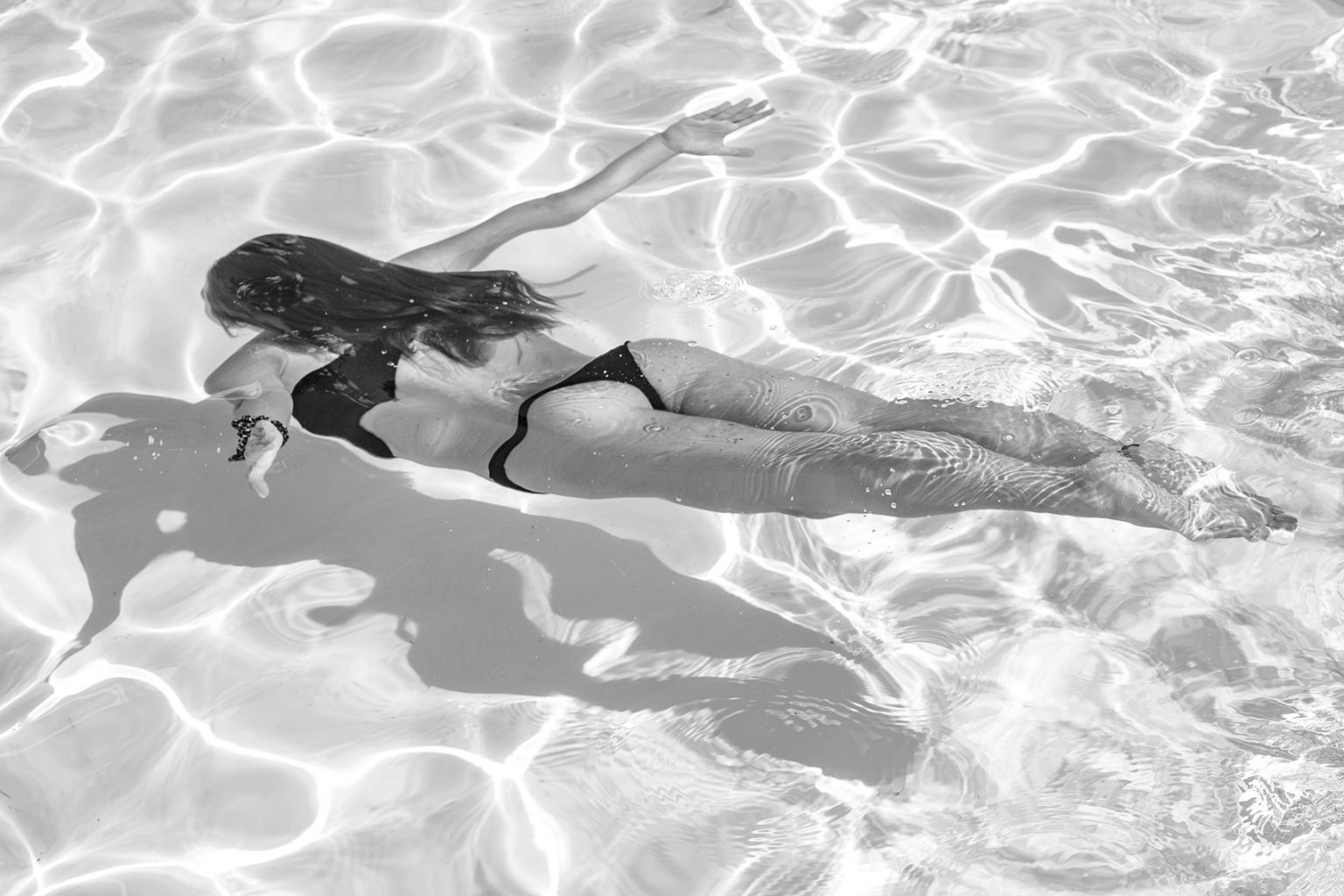 photo noir et blanc d'une femme en bikini noir qui plonge dans l'eau clair